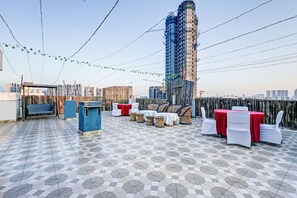 Una terraza en la azotea con suelo estampado, mobiliario exterior y vistas a un edificio alto en construcción.