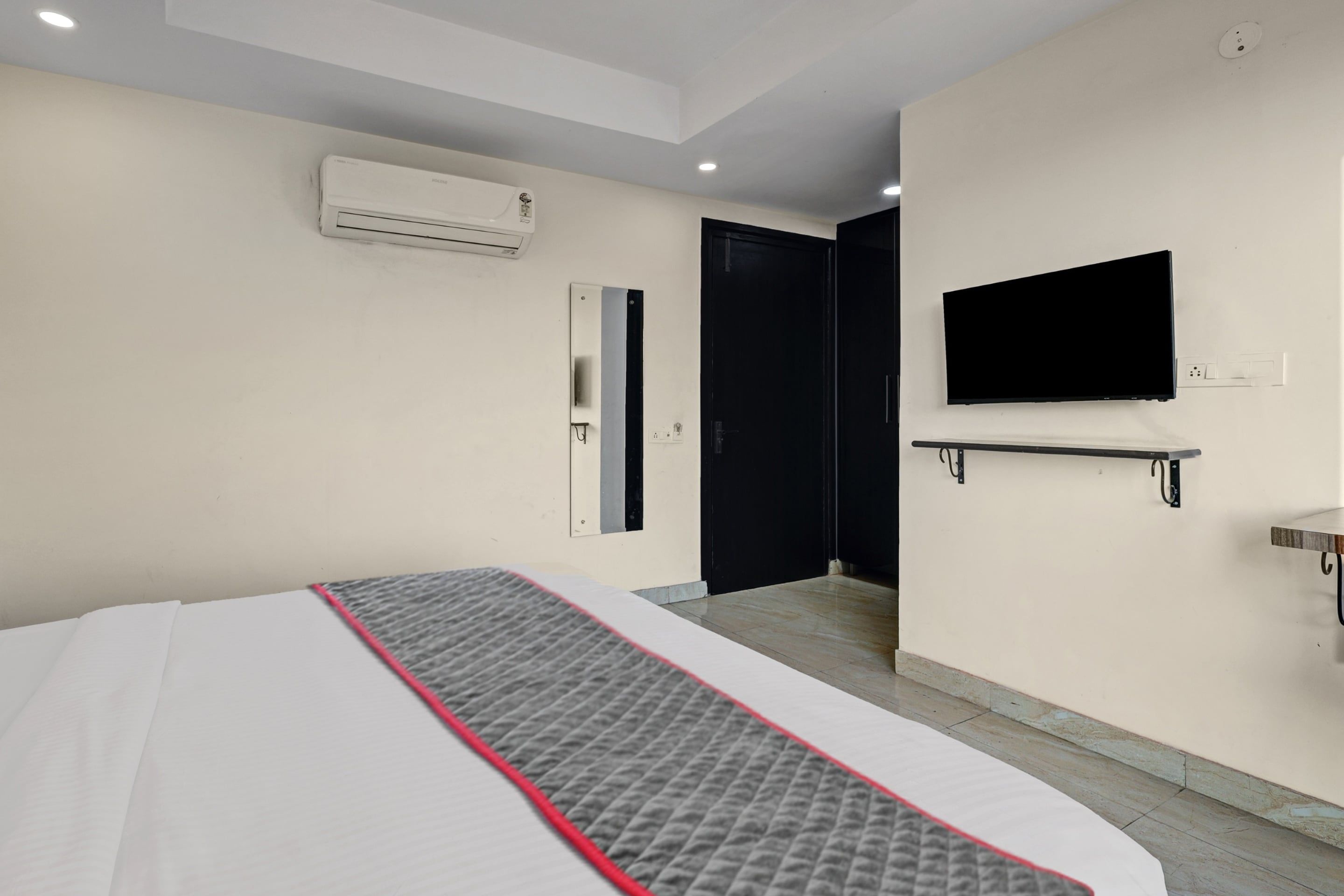 Quarto de hotel com cama, ar condicionado, televisão fixada na parede e porta que dá para outro quarto.