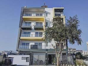 Un edifici residencial de diversos pisos amb balcons, una entrada tancada i un arbre al primer terme.