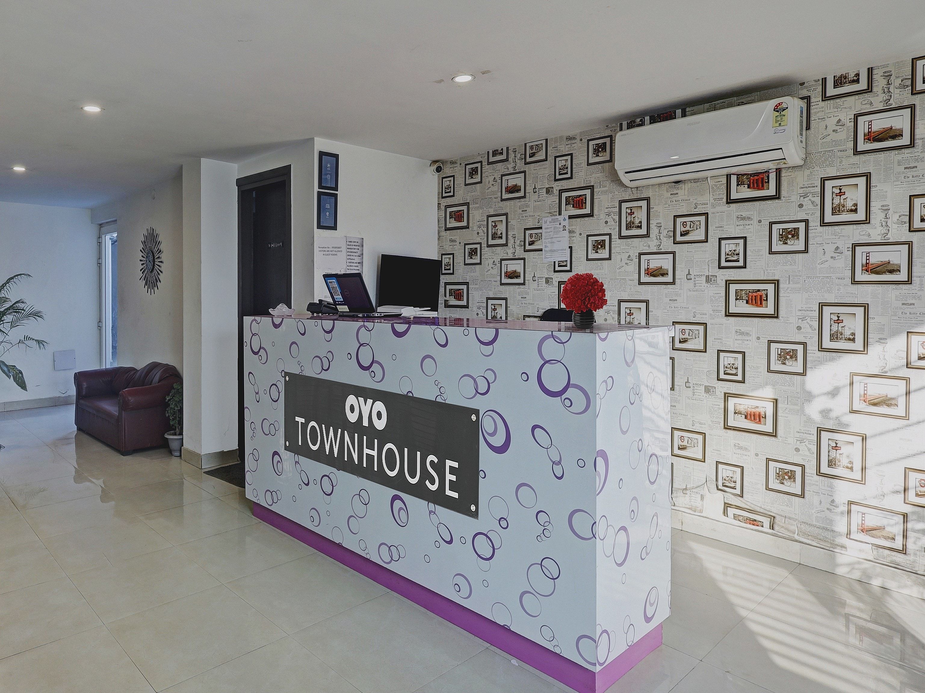 A reception desk with a sign reading 'OYO TOWNHOUSE' and a patterned wall with framed pictures.