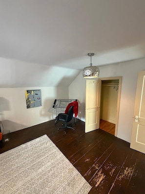 A room with a dark wooden floor, a white rug, a black office chair with a red throw, a ceiling light fixture, and a door leading to another room. - Welcome home ! 
West end of Halifax, 3 bedroom home is waiting for you! (Halifax)