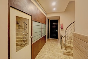 Un pasillo con una puerta de madera, una puerta de vidrio con marco de metal y una escalera con barandillas metálicas.