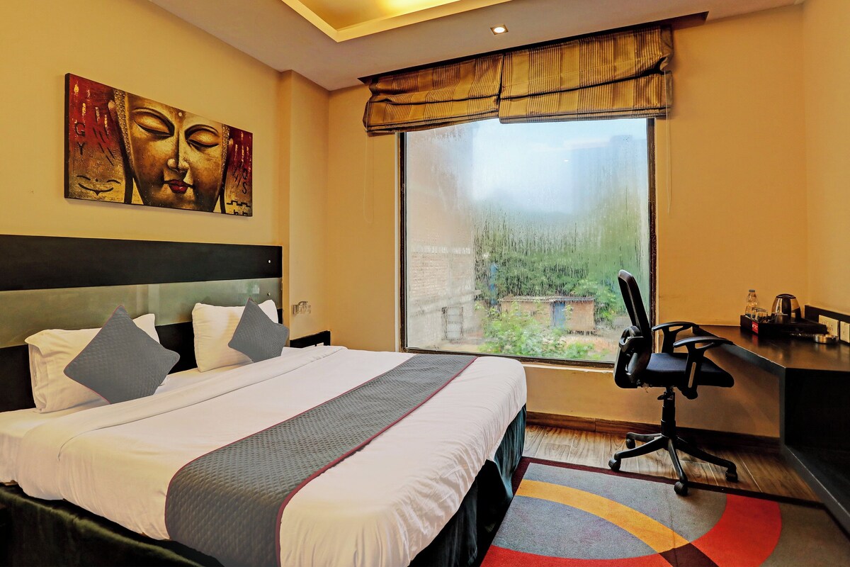 Una habitación de hotel con cama, escritorio, silla, un ventanal grande y obras de arte en la pared.