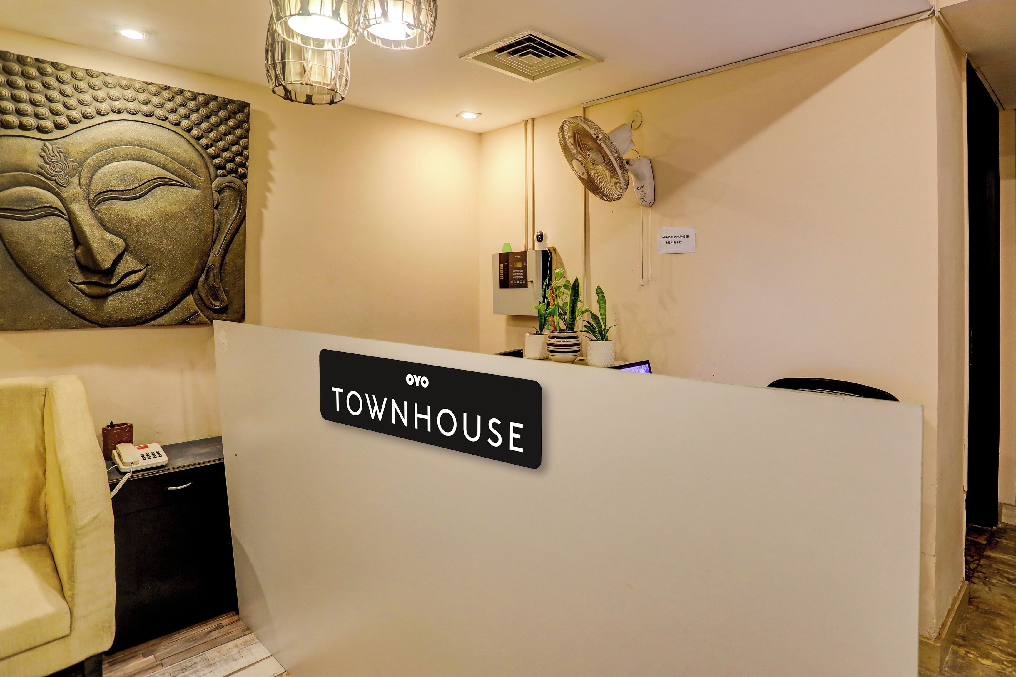 Un comptoir d’accueil avec une enseigne indiquant « OYO TOWNHOUSE », un téléphone fixé au mur, une petite plante et un luminaire au plafond.