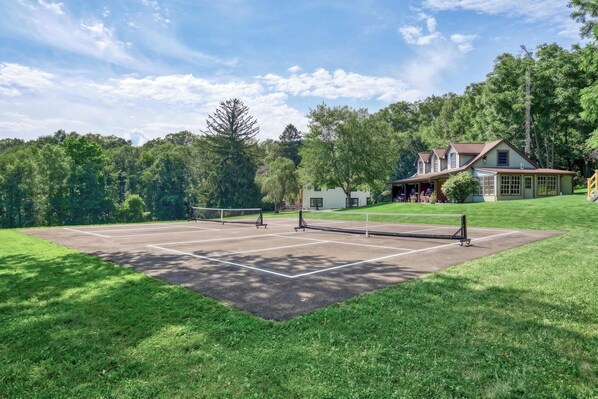 Una cancha de tenis con red, rodeada de césped y árboles.