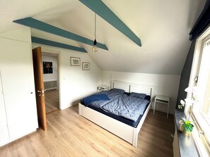 A bedroom with a sloped ceiling, a bed with a patterned bedspread, a bedside table, and a potted plant by the window. - A Småland idyll, 300 m from the lake – patio & tranquility (Ryd)
