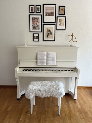 A piano with sheet music, a fluffy white bench, and framed artwork on the wall. - A Småland idyll, 300 m from the lake – patio & tranquility (Ryd)