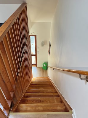 A wooden staircase with a handrail, leading to a room with a door and a wall-mounted light fixture. - A Småland idyll, 300 m from the lake – patio & tranquility (Ryd)