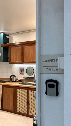 A kitchen with wooden cabinets, a sink, and a wall-mounted soap dispenser. - Cozy 2BR Private Home in Central Hanoi Old Quarter - Kichen, Washer, Wifi & AC (Hoan Kiem)