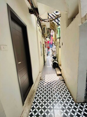 A narrow corridor with patterned flooring, a door on the left, and a scooter parked on the right. - Cozy 2BR Private Home in Central Hanoi Old Quarter - Kichen, Washer, Wifi & AC (Hoan Kiem)