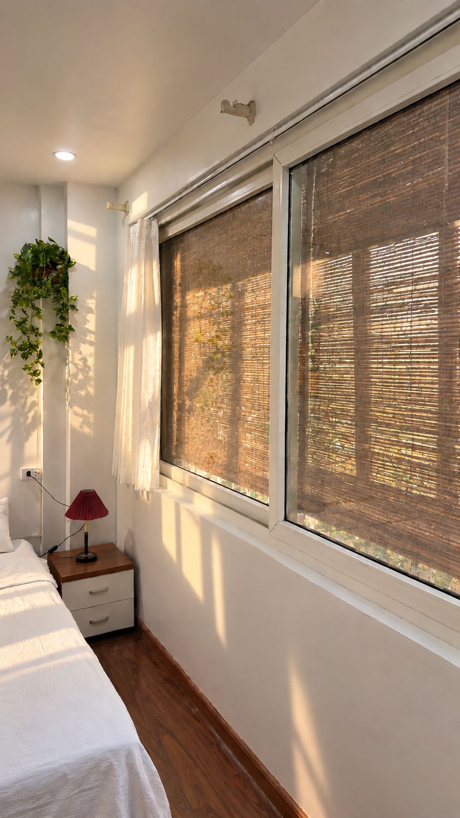 A bedroom with a bed, bedside table, lamp, and a window with blinds.