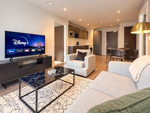 Una sala de estar moderna con un televisor de pantalla plana mostrando Disney+, un sofá, una mesa de centro y un comedor con sillas.