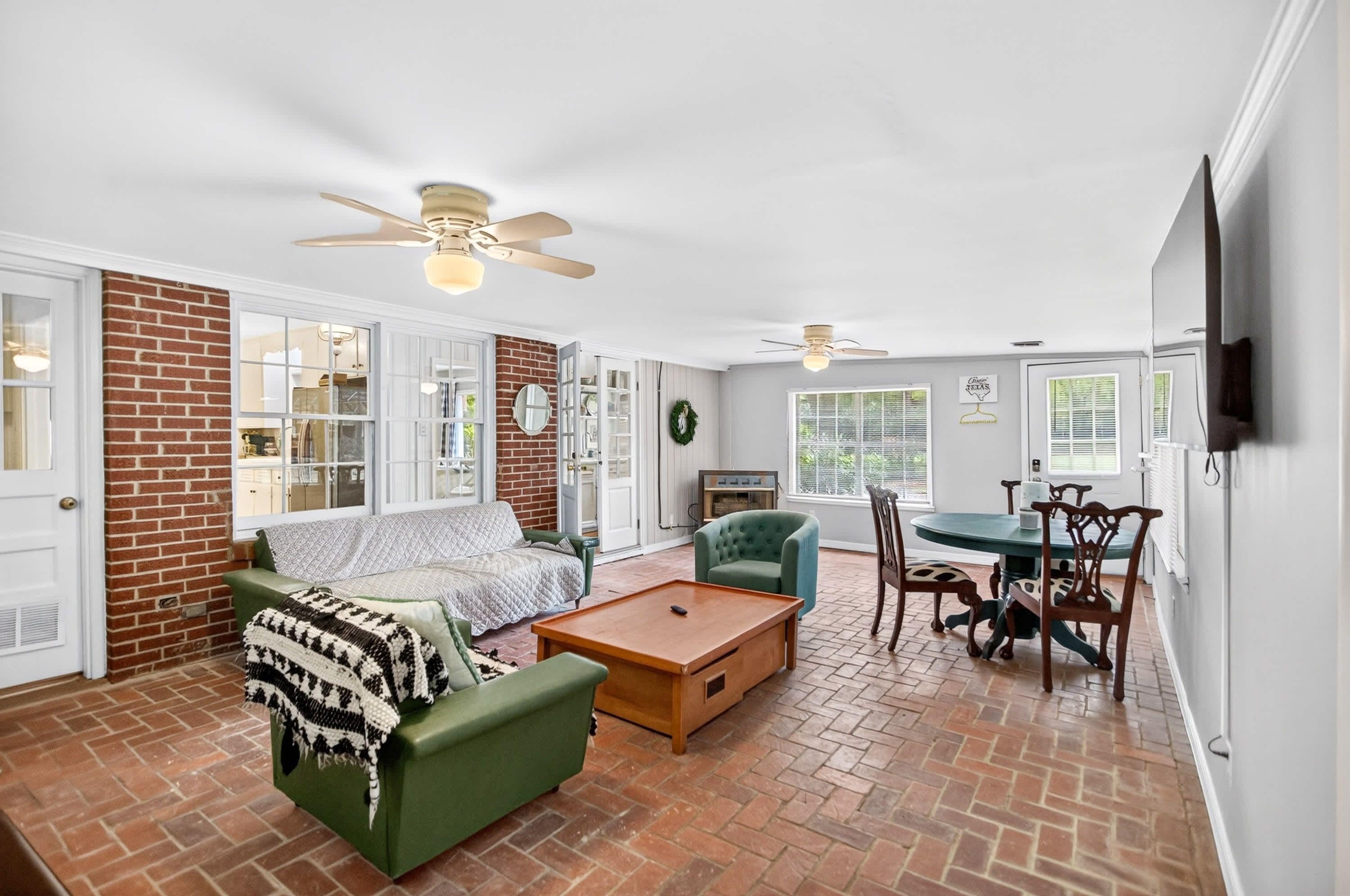 A spacious living room with a brick fireplace, a green sofa, a wooden coffee table, and a dining area with a table and chairs.