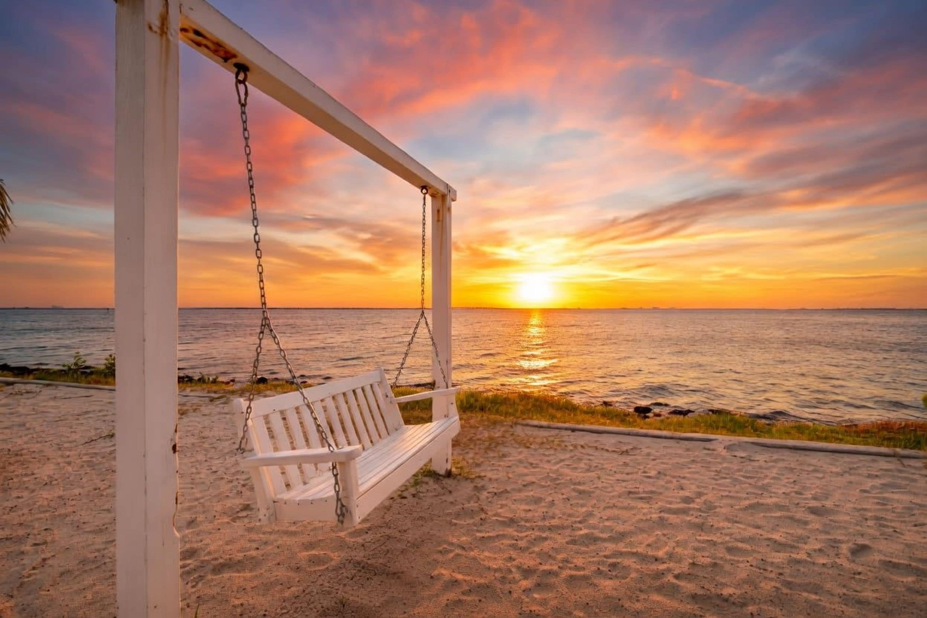 Una playa con un conjunto de columpios y una puesta de sol sobre el océano.