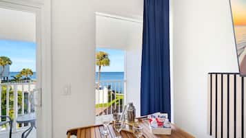 Ein Zimmer mit einem Holztisch, einem Fenster mit Meerblick und einem Vorhang.
