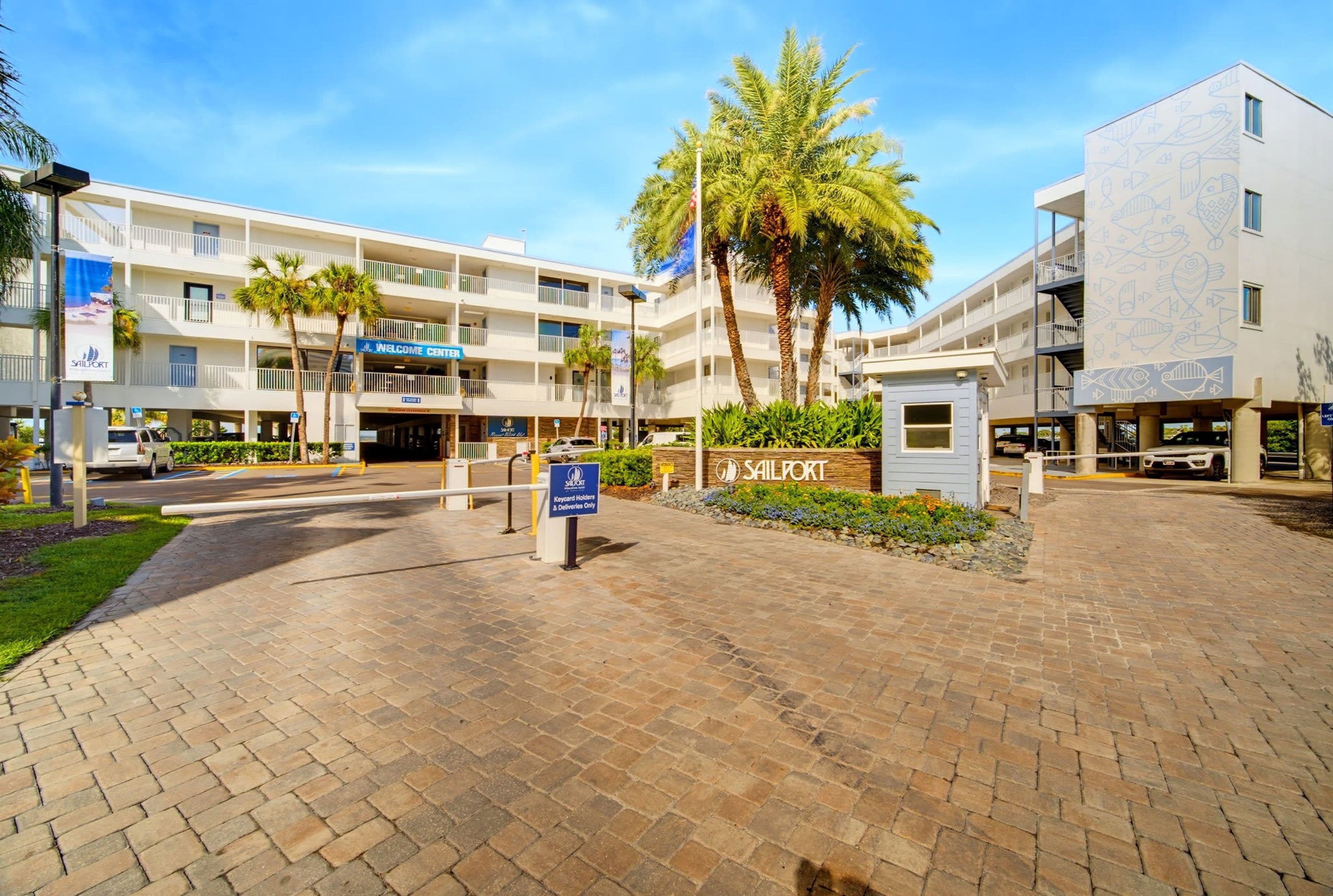 Un hotel de varios pisos con un patio central, palmeras y un letrero que indica zona de entrega de tarjetas electrónicas.