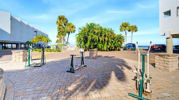 An outdoor exercise area with fitness equipment, a paved walkway, and a view of a building and palm trees.