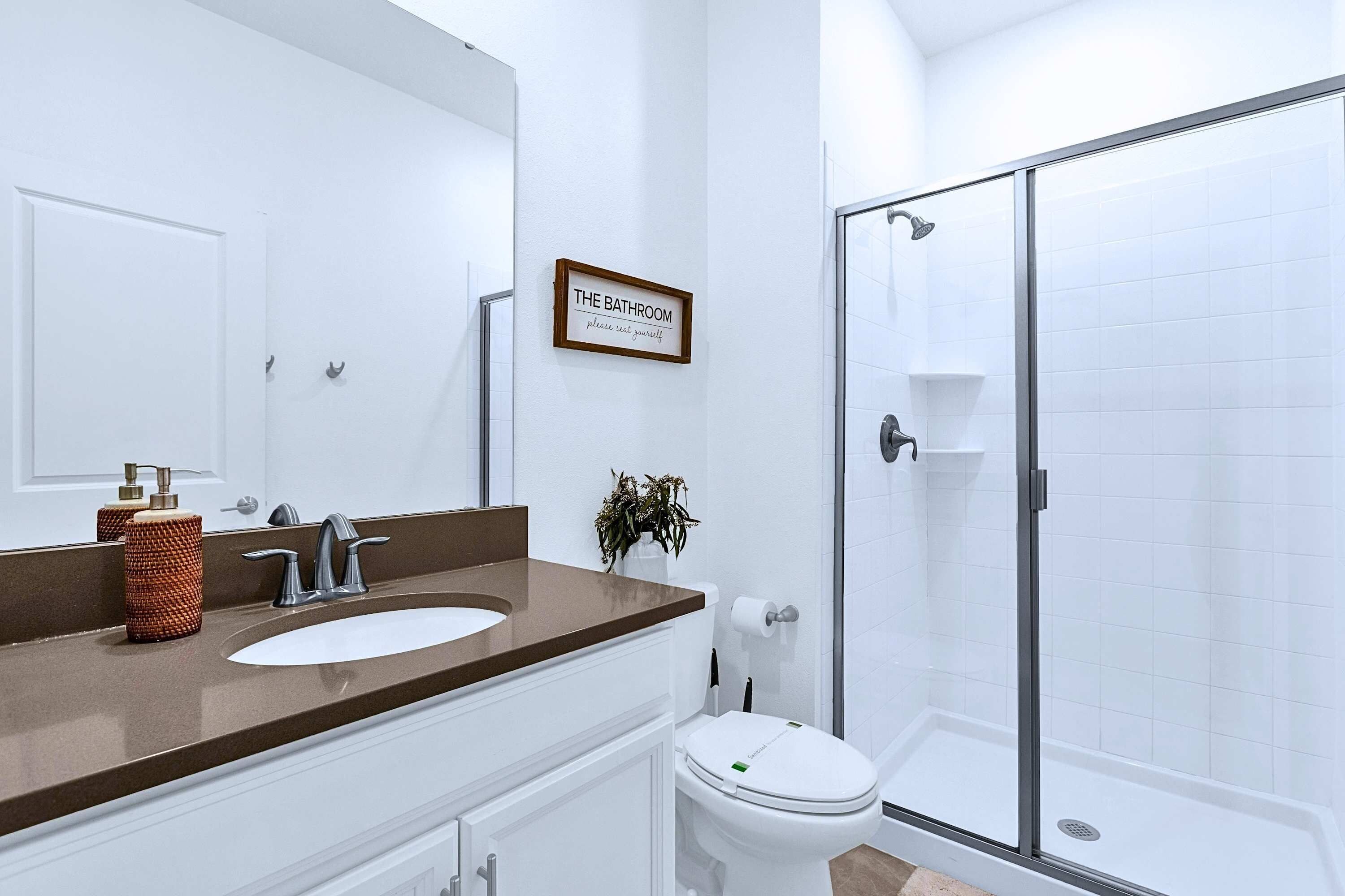 Ein Badezimmer mit einem weißen Waschbecken, einem Spiegel, einer Toilette und einer Duschkabine.