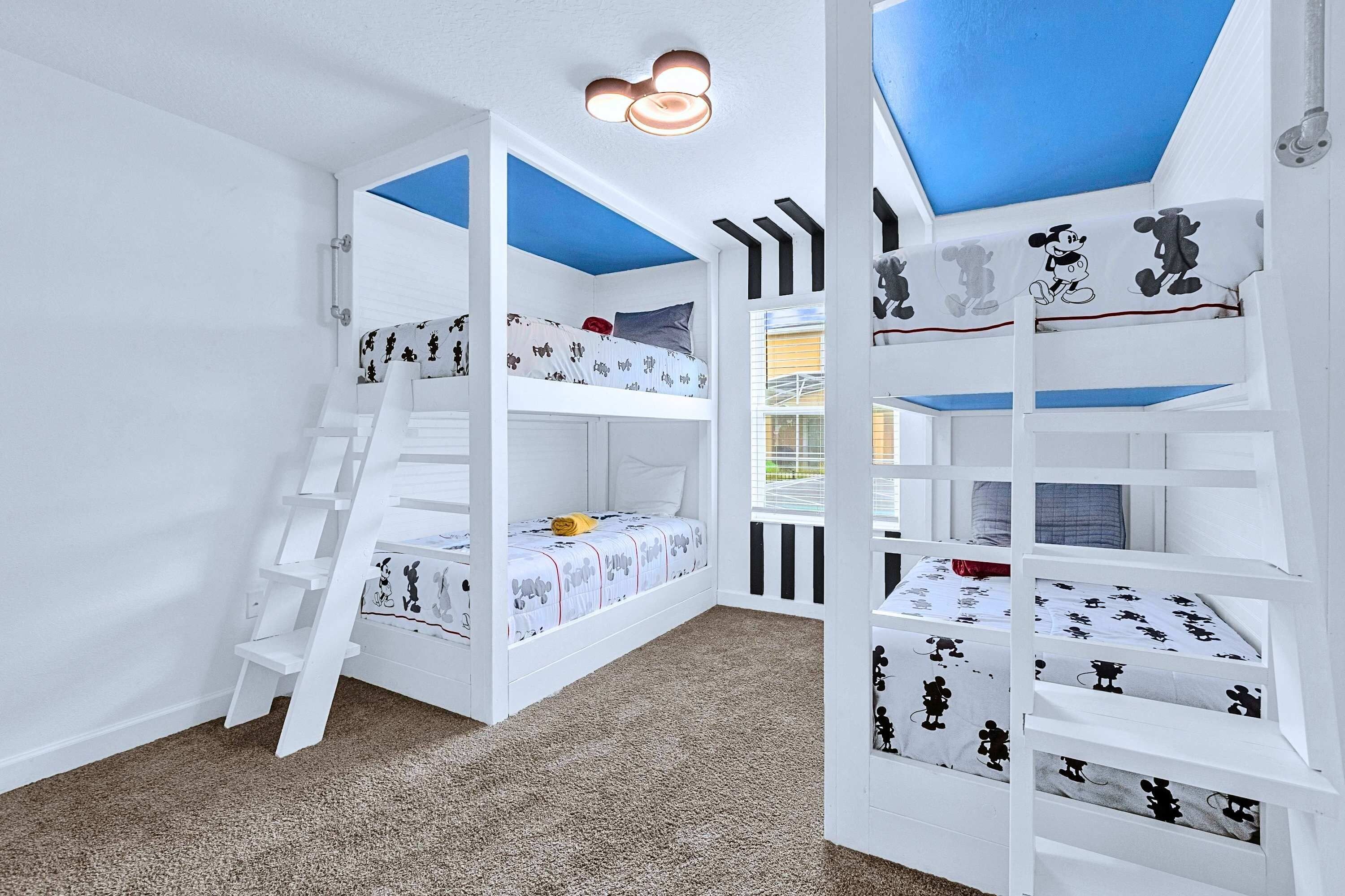 A children's bunk bed room with a ladder, white walls, and a window with blinds.