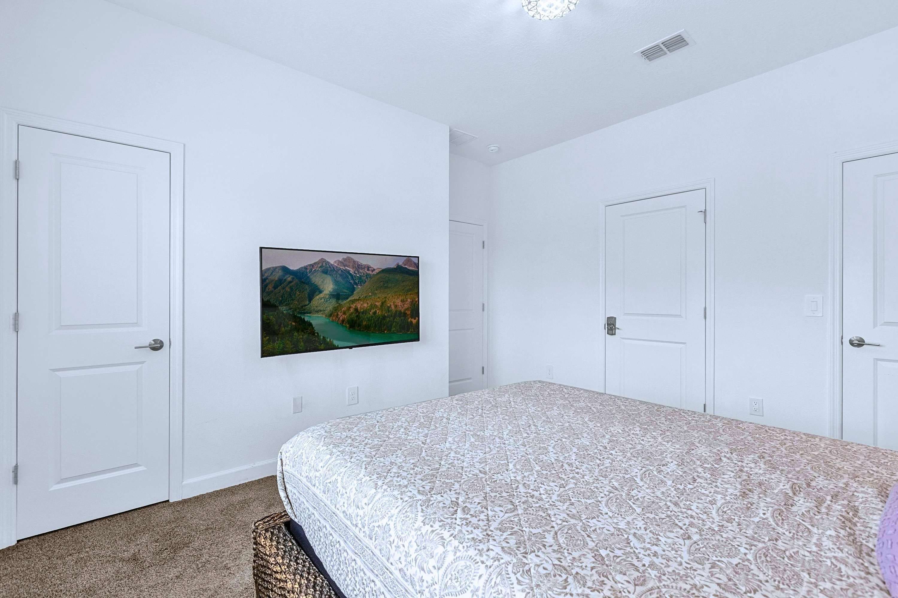 A bedroom with a bed, two doors, a wall-mounted picture, and a carpeted floor.