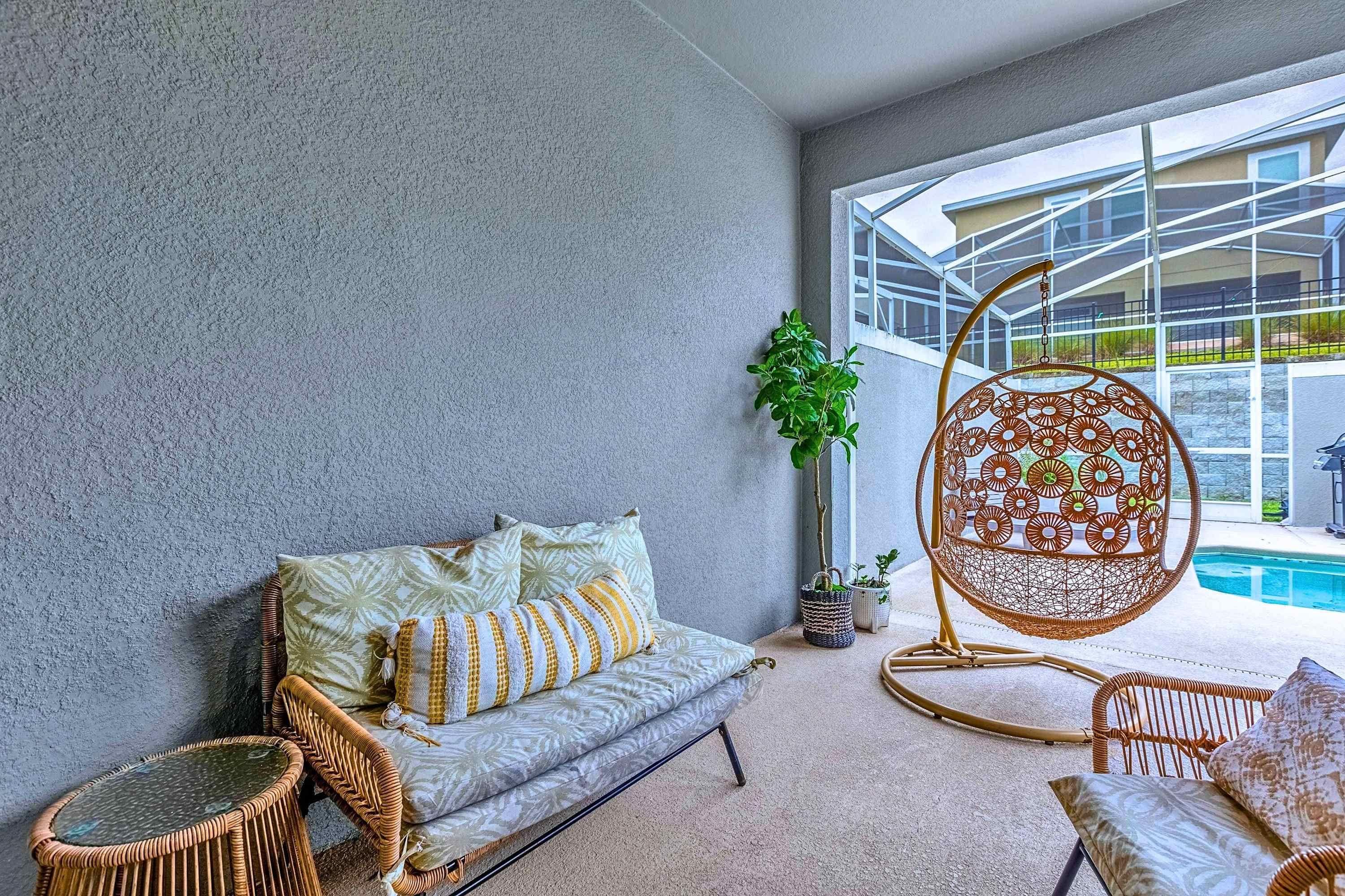 Un área de descanso moderna con una pared gris texturizada, un sofá con cojines estampados, un sillón colgante y una planta en maceta.