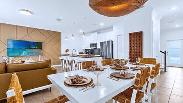 A modern living room with a sofa, dining table set for six, and a kitchen in the background.