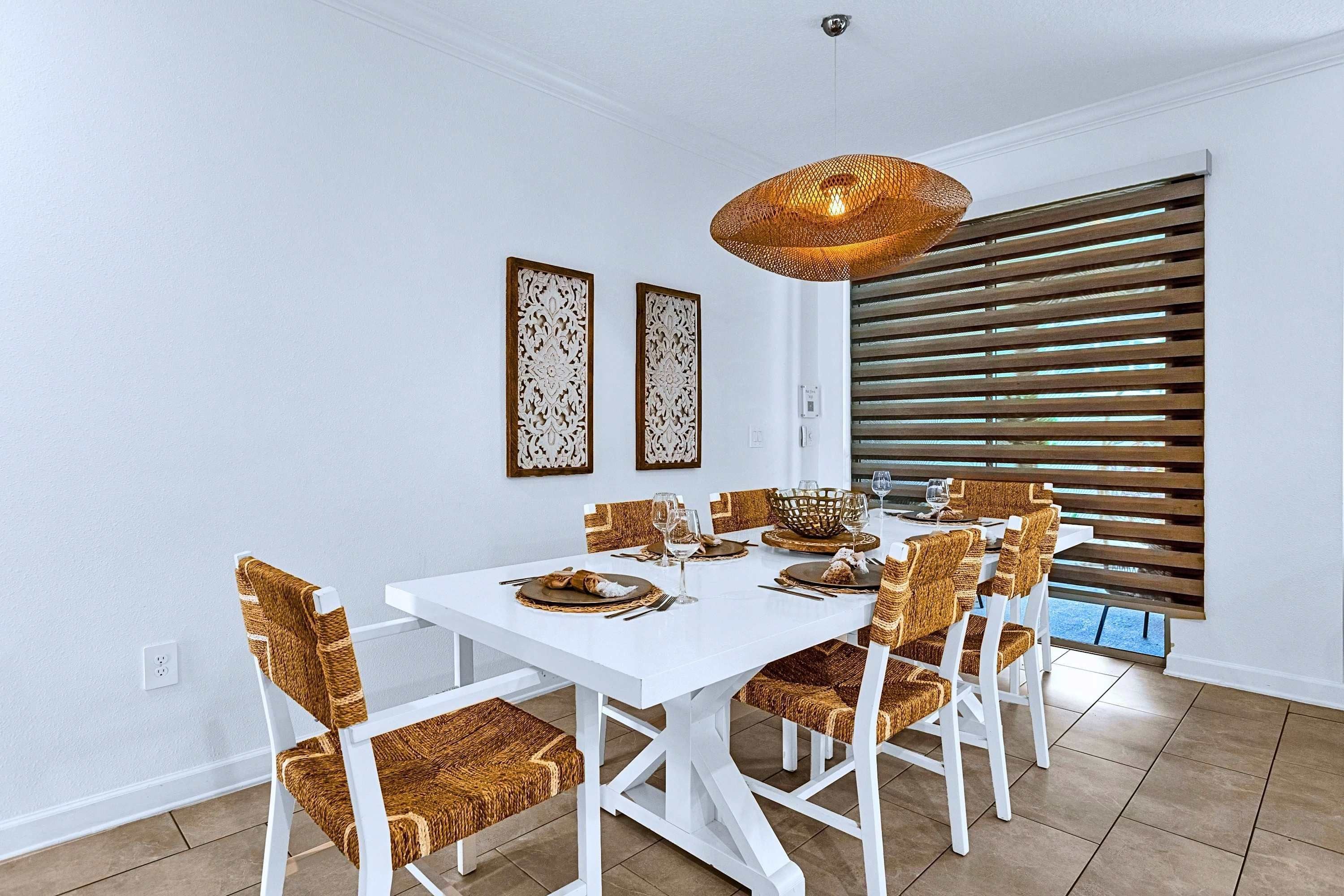 A dining area with a white table, wicker chairs, and a woven pendant light.