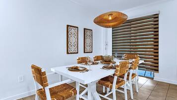 A dining area with a white table, wicker chairs, and a woven pendant light.