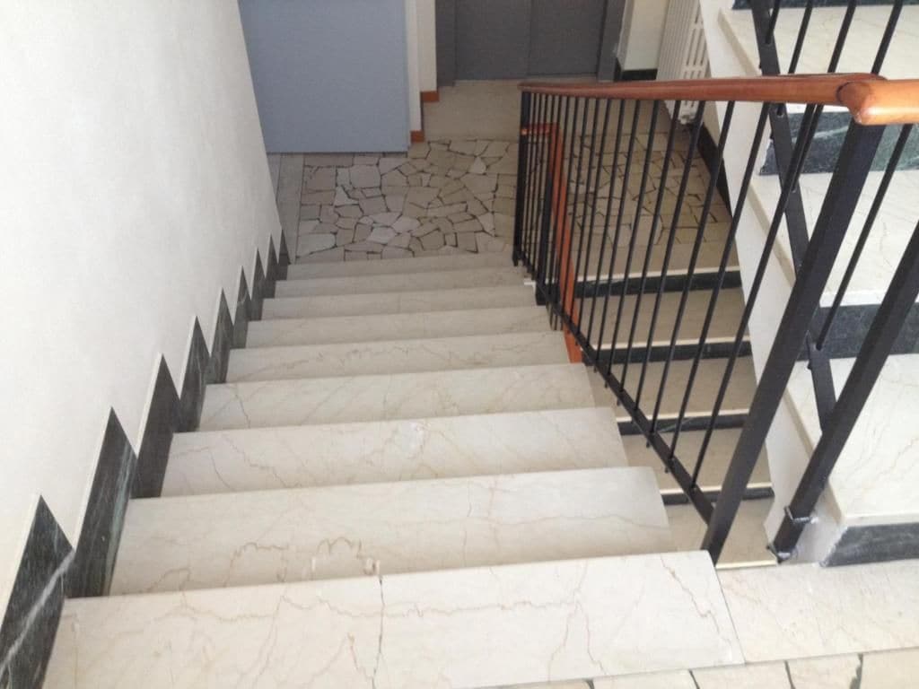 Un escalier avec des marches en marbre et une rampe en métal noir.