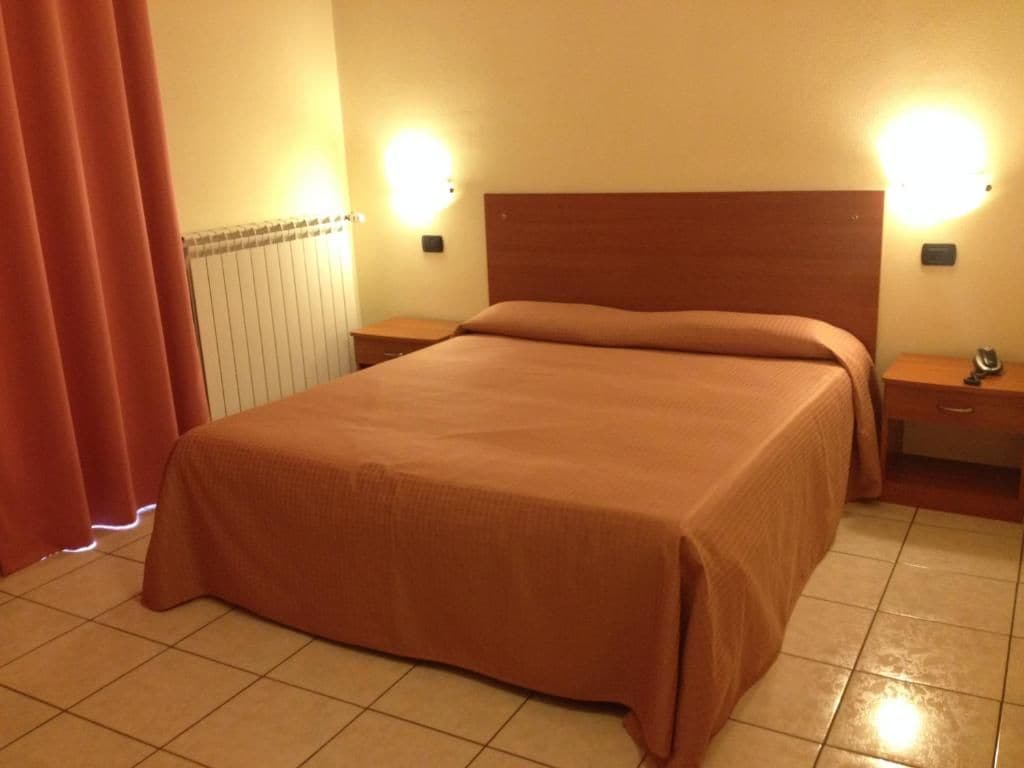 Habitació d'hotel amb un llit gran, dues taules de nit i un radiador.
