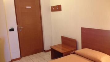 Una habitación con una cama, una mesita de noche de madera, una puerta y un gancho fijado a la pared.