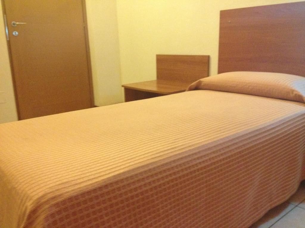 Ein Einzelbett mit Holz Kopfteil und Nachttisch daneben.