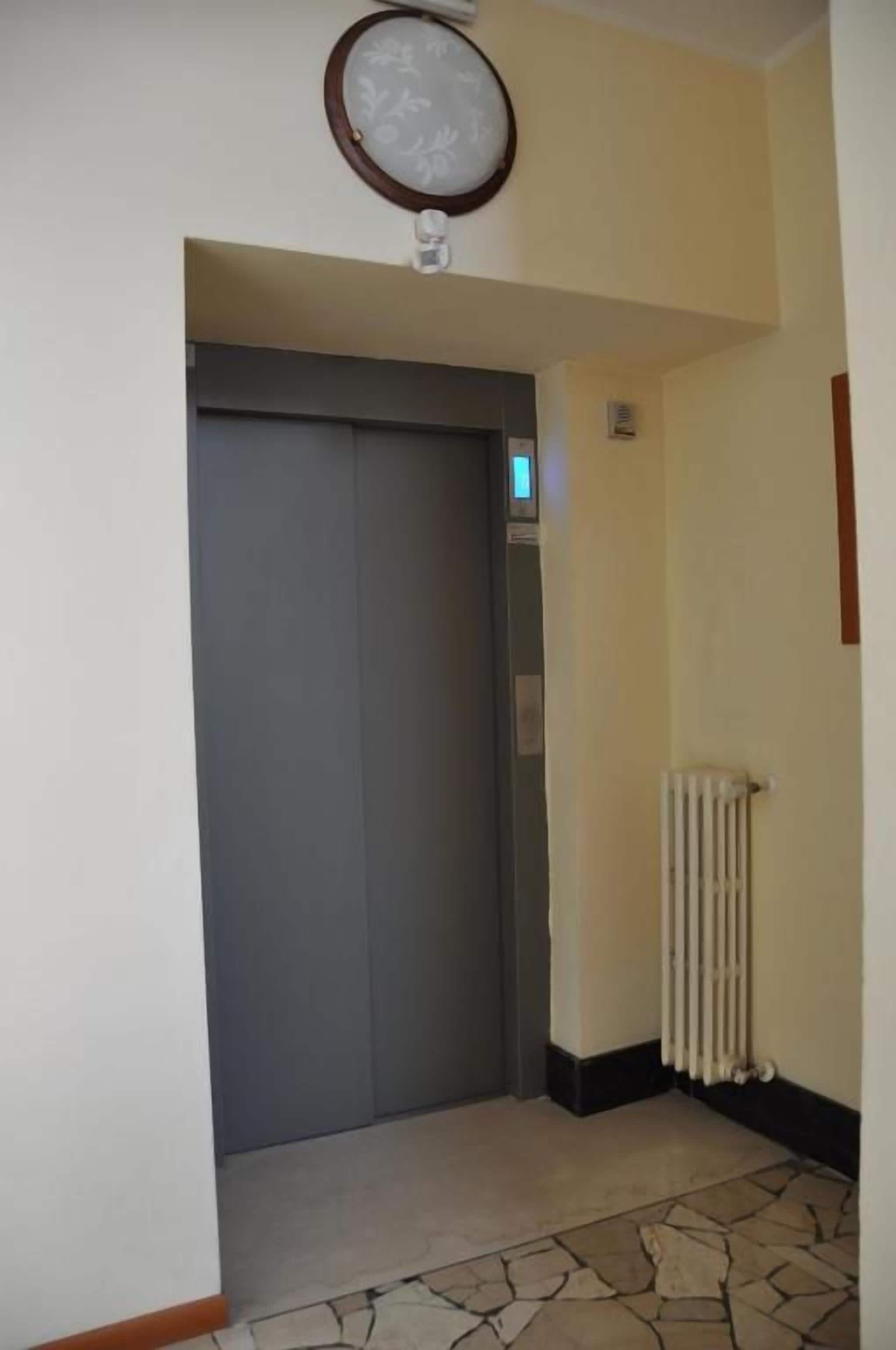Un couloir avec une porte de monte-charge fermée, un radiateur et un sol à motifs.