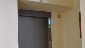 Un couloir avec une porte de monte-charge fermée, un radiateur et un sol à motifs.