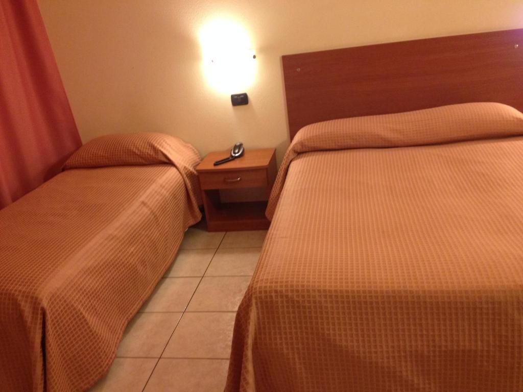 Ein Hotelzimmer mit zwei Betten, einem Nachttisch, einer Lampe und Wandleuchten.