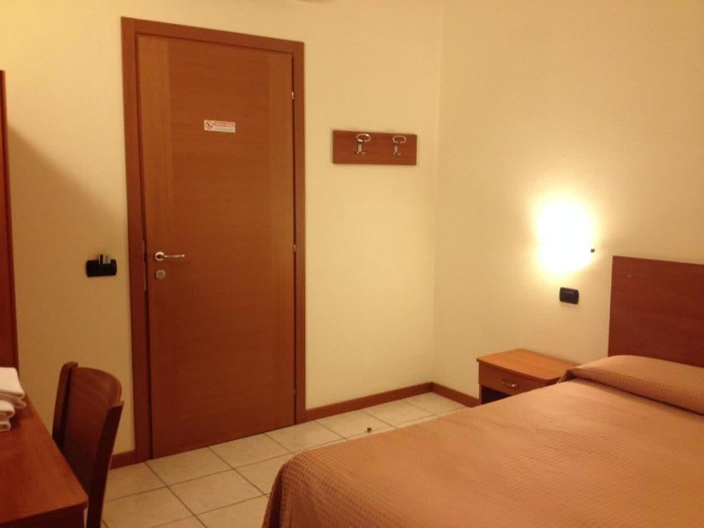 Una camera d'albergo con un letto, una scrivania, una sedia, una porta e un lampadario a parete.