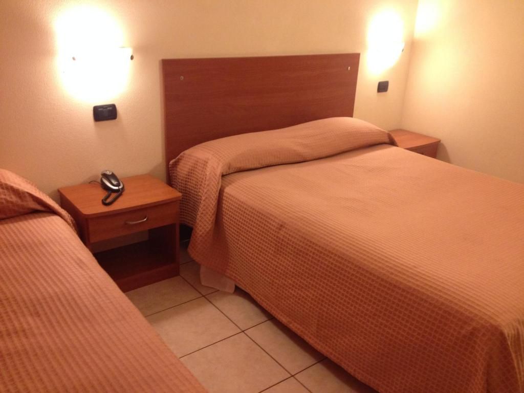 Una habitación de hotel con dos camas, una mesita de noche, un teléfono e iluminación en la pared.