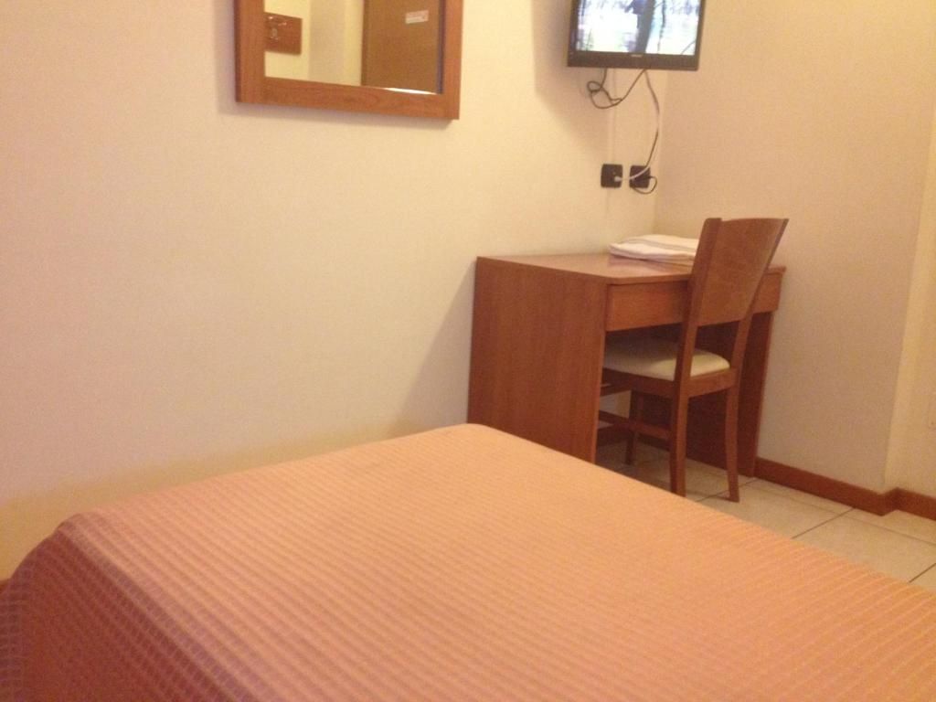 Une chambre d’hôtel équipée d’un lit, d’un bureau, d’une chaise et d’un téléviseur fixé au mur.
