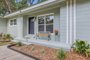 Ein eingeschossiges Haus mit Veranda, einer Bank und einem Blumentopf.