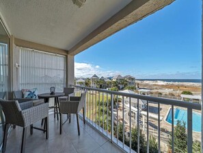 A balcony with wicker furniture, a view of a beach, and a swimming pool. - Destin Pointe Magnolia House #306 | Luxe Condo, Beautiful Views + Amenities (Destin)