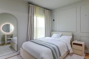 Ein Schlafzimmer mit Bett, Nachttisch, Spiegel und einem Fenster mit Vorhängen.