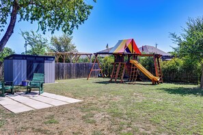 A backyard with a wooden play structure, a covered seating area, and a fenced yard. - Fenced Yard & Playset Near SA Airport & Parks (San Antonio)