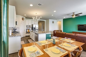 A modern kitchen with white cabinets, a central island, and a dining area with a wooden table set for four. - Fenced Yard & Playset Near SA Airport & Parks (San Antonio)