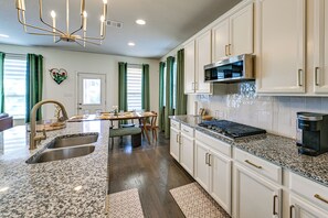 A modern kitchen with granite countertops, stainless steel appliances, and a dining area with a table and chairs. - Fenced Yard & Playset Near SA Airport & Parks (San Antonio)