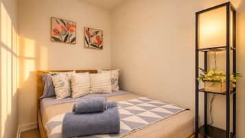 A bedroom with a bed, pillows, a bedside table with a lamp, and two wall-mounted flower paintings.