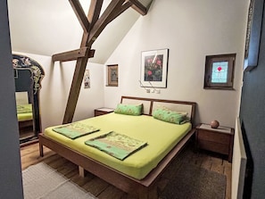Un dormitorio con techo inclinado, una cama con ropa de cama verde, un cabecero de madera y dos mesitas de noche.