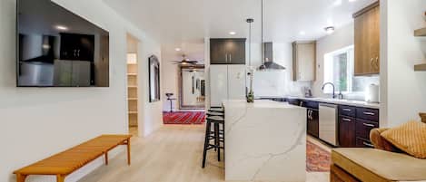 A modern kitchen with a central island, a dining area with a bench, and a living space with a sofa and a TV.