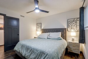 Une chambre à coucher avec un lit, une table de chevet, un ventilateur de plafond et des œuvres d’art accrochées aux murs.