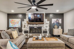 Un salon doté d’une cheminée en pierre, d’un ventilateur de plafond et d’un téléviseur à écran plat fixé au-dessus de la cheminée.
