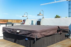Een dak met een overdekte hottub, twee buitenlampen en een houten terras.